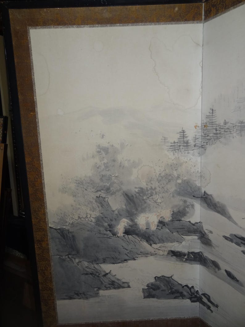 May include: A framed, multi-panel artwork featuring a landscape scene. The artwork depicts a mountainous terrain with trees and water, rendered in shades of gray and white. The frame is a dark brown color.