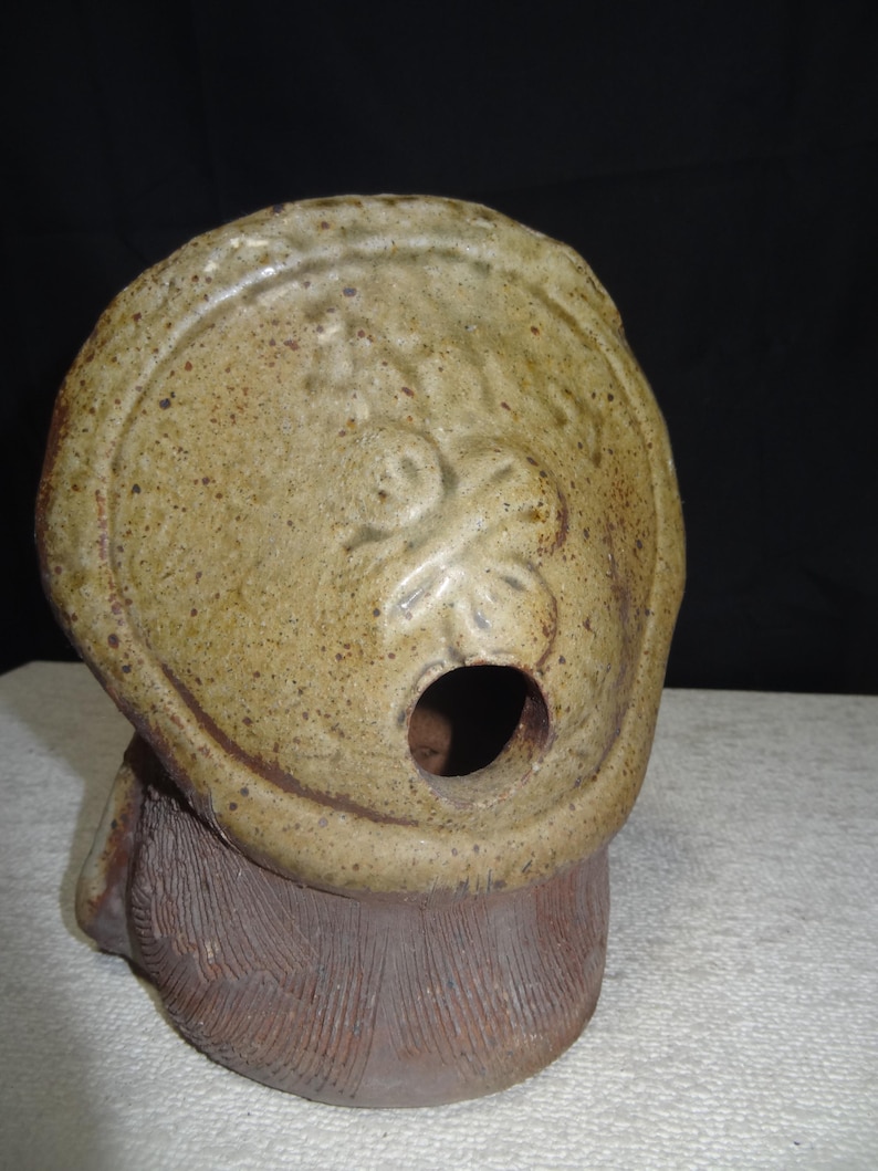 May include: A ceramic sculpture of a tanuki, a Japanese raccoon dog. The sculpture has a round head with a large opening and a textured body. The tanuki is a traditional figure in Japanese folklore, often associated with good fortune and prosperity.