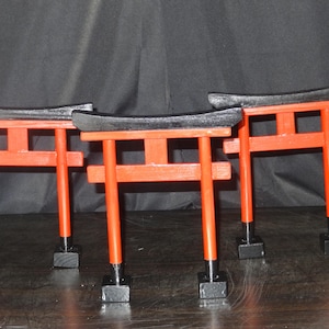 以下が含まれることがあります： 伝統的な日本の神道神社である、3つのミニチュア鳥居。 門は鮮やかな赤色で塗装され、上部とベースに黒のアクセントが付いています。 門は暗い表面に表示されています。