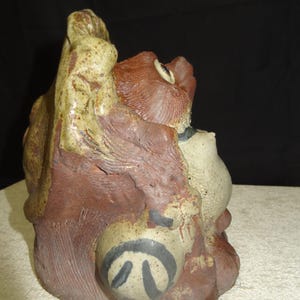May include: A ceramic sculpture featuring a stylized animal figure. The sculpture is primarily brown and beige with black accents. The figure has a textured surface and a unique, abstract design.