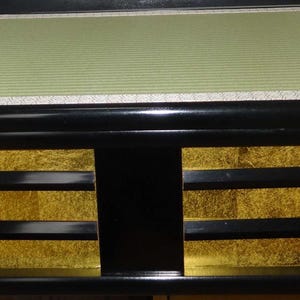 May include: A low, rectangular Japanese-style platform bed. The bed features a black frame with gold-colored panels and a light green, textured top. The design is simple and elegant, suitable for a minimalist bedroom.