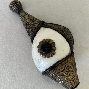 May include: An antique, ornate, ivory-colored object with metal accents. The object has a bulbous shape with intricate metalwork at both ends and a decorative floral element in the center. The metal appears to be silver or a silver-toned alloy.