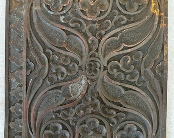 May include: A decorative metal plate with an intricate floral design. The plate is a dark brown color with a slightly green patina. There are two small holes in the plate.