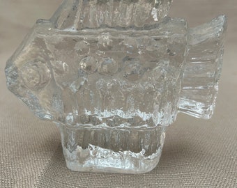 May include: A clear glass fish-shaped candle holder with a textured surface. The holder has a small opening on the top for a candle.