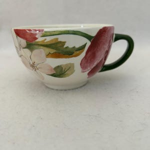 Puede incluir: Taza de té de cerámica blanca con un diseño floral con flores rojas y rosas, hojas verdes y un asa verde. La taza tiene una forma ancha y poco profunda, adecuada para té o café. El estampado floral está pintado a mano.