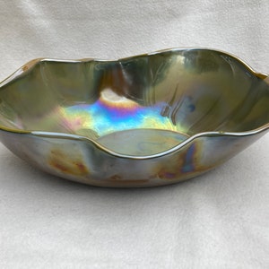 May include: A large, iridescent, green glass bowl with a wavy, scalloped rim. The bowl has a metallic sheen and reflects light in a rainbow of colors.