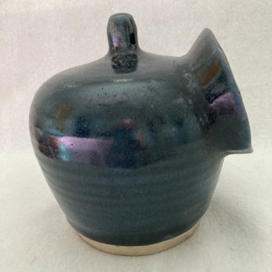 May include: A dark blue ceramic salt cellar with a wide opening and a small spout. The cellar has a light brown rim and a glossy finish.