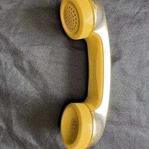 May include: A vintage yellow and silver rotary phone handset with a round, textured mouthpiece and earpiece.