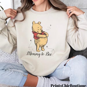 May include: A beige sweatshirt with a Winnie the Pooh illustration and the text "Mommy to Bee".
