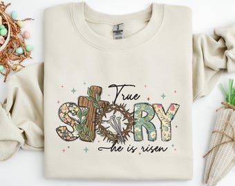 May include: A beige sweatshirt with a floral design that spells out "TRUE STORY" with a crown of thorns and nails. The text below reads "He is risen".