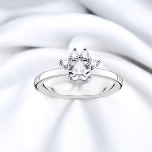 Könnte beinhalten: Ein silberner Ring mit einem klaren Kristall-Pfotenabdruck-Design. Der Ring liegt auf einem weißen Hintergrund.