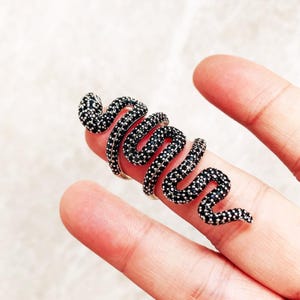Könnte beinhalten: Ein silberner Schlangenring mit schwarzen Steinen. Die Schlange ist um den Finger gewickelt und hat ein detailliertes Design.