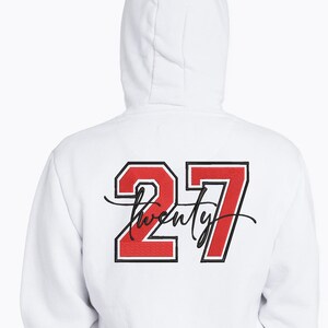 May include: White hooded sweatshirt with the number "27" in red with a black outline. The word "twenty" is written in a cursive font below the number. The sweatshirt is a casual style.