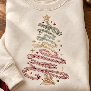 May include: An off-white crewneck sweatshirt featuring an embroidered design of the word Merry arranged in a triangular Christmas tree shape. The embroidery uses gradient thread colors of green, gold, and red, accented with small gold stars and dots.