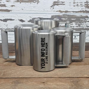 May include: A collection of four stainless steel mugs with textured handles. The smallest mug has the text "YOUR INFO HERE 2 LINE MAXIMUM" printed on the side. The mugs are cylindrical with a wide opening.