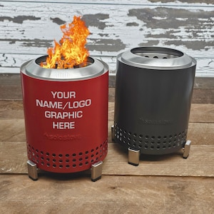 May include: Two cylindrical fire pits. One is red with the text "YOUR NAME/LOGO GRAPHIC HERE" in white, and the other is black. Both have a silver rim and small metal legs. The red fire pit has a fire burning inside.