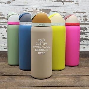 May include: A collection of insulated water bottles in various colors, including green, blue, tan, yellow, and pink. Each bottle has a unique lid design and the word "owala" printed on the band. The tan bottle features the text "YOUR CUSTOM IMAGE/LOGO MESSAGE HERE."