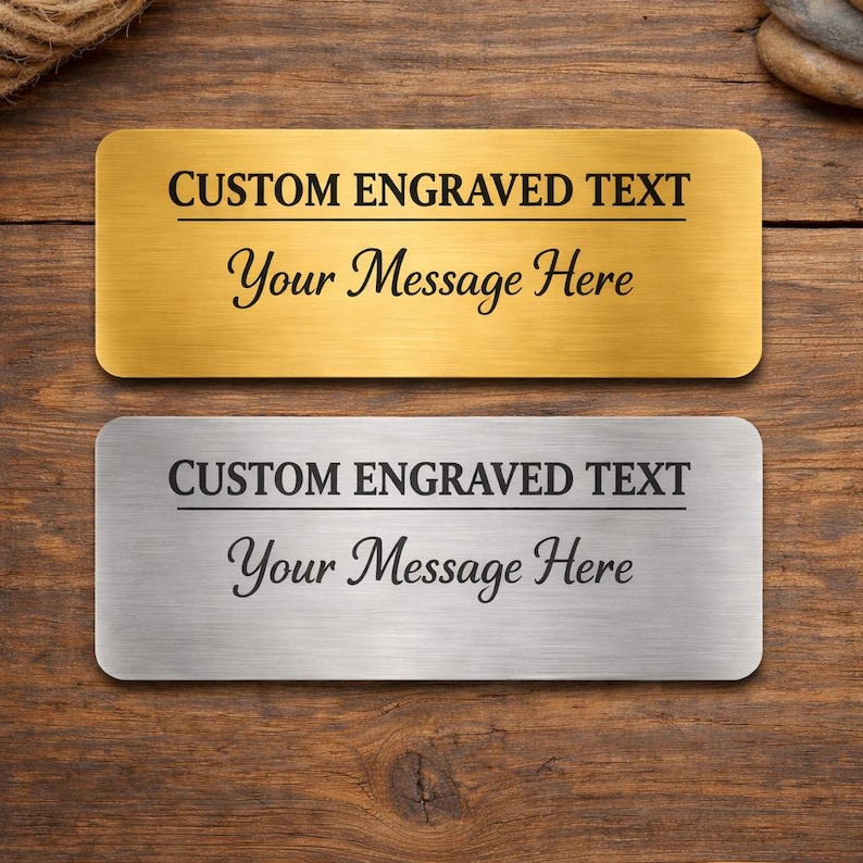 Puede incluir: Dos placas de identificaci&oacute;n rectangulares, una dorada y otra plateada, con esquinas redondeadas. Cada placa tiene el texto "CUSTOM ENGRAVED TEXT" encima de "Your Message Here" en una fuente cursiva. El fondo es una superficie de madera.