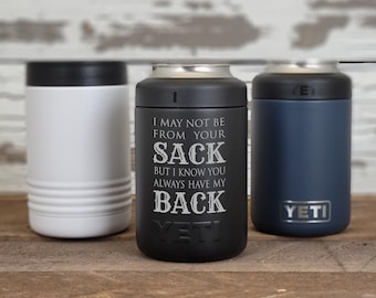 May include: Three insulated can coolers in white, black, and navy blue. The black cooler has the text "I MAY NOT BE FROM YOUR SACK BUT I KNOW YOU ALWAYS HAVE MY BACK YETI". The navy blue cooler has the "YETI" logo.