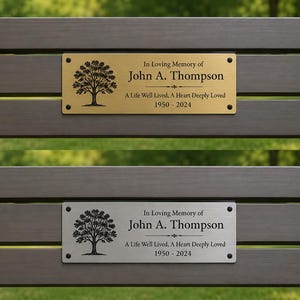 May include: A rectangular metal memorial plaque attached to a dark brown wooden bench. The plaque features a black tree graphic, the text In Loving Memory of John A. Thompson, A Life Well Lived, A Heart Deeply Loved, and the years 1950-2024.
