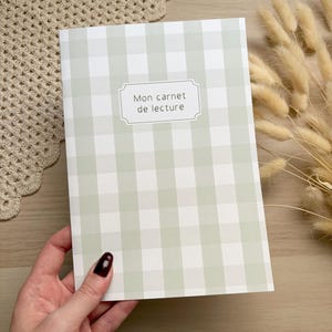 Peut inclure: Un carnet de lecture rectangulaire avec un motif à carreaux vichy vert sauge clair et blanc. Une étiquette blanche centrale avec une bordure décorative affiche le texte Mon carnet de lecture dans une police sans empattement simple.
