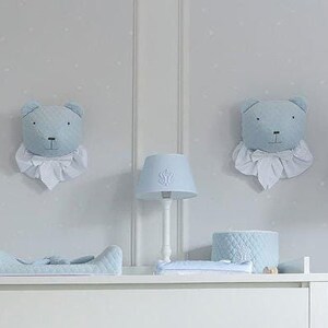 Peut inclure: Une chambre de bébé décorée en blanc et bleu clair. On y trouve un lit bébé, une commode et un cheval à bascule. Des décorations murales en forme de têtes d'ours sont présentes. Le cheval à bascule a une selle grise. L'ensemble évoque une ambiance douce et enfantine.