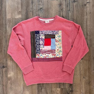 Peut inclure: Un sweat-shirt à manches longues de couleur corail avec un empiècement carré central composé de divers morceaux de tissu à motifs floraux, rayés et à pois. Le vêtement présente un col rond, des poignets et un ourlet côtelés.