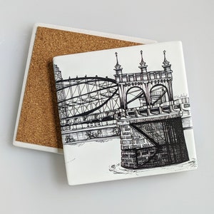 May include: Black and white line drawing of a bridge with a detailed design. The bridge is made of metal and has a series of arches. The drawing is on a white ceramic coaster with a cork backing.