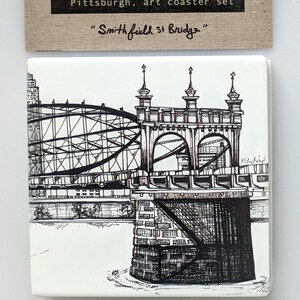 May include: Black and white line drawing of the Smithfield Street Bridge in Pittsburgh, Pennsylvania. The drawing is on a white ceramic tile coaster. The text "Pittsburgh, art coaster set" and "Smithfield St Bridge" is printed on the coaster.