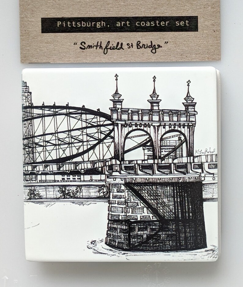May include: Black and white line drawing of the Smithfield Street Bridge in Pittsburgh, Pennsylvania. The drawing is on a white ceramic tile coaster. The text "Pittsburgh, art coaster set" and "Smithfield St Bridge" is printed on the coaster.