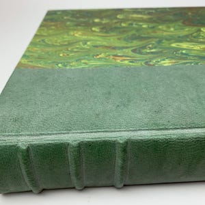 May include: A hardback book featuring a textured, matte sage green spine with four raised bands. The cover displays a marbled pattern in shades of lime green, forest green, and hints of brown, creating a fluid, swirling design across the surface.
