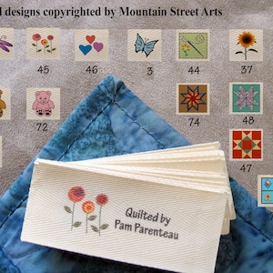 May include: A collection of small fabric squares with embroidered designs, including flowers, butterflies, and bears. The text "All designs copyrighted by Mountain Street Arts" is at the top. A stack of labels reads "Quilted by Pam Parenteau".