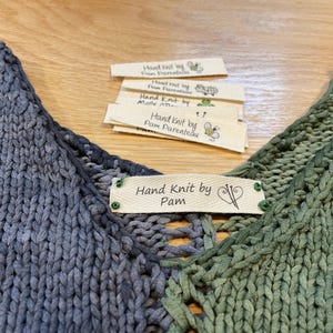 May include: A hand-knitted garment with a blue and green ombre color scheme. The garment has a label that reads "Hand Knit by Pam".