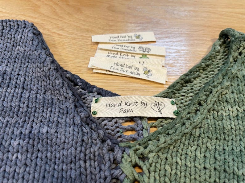 May include: A hand-knitted garment with a blue and green ombre color scheme. The garment has a label that reads "Hand Knit by Pam".