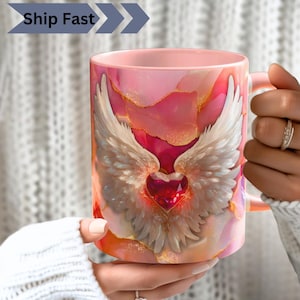 Könnte beinhalten: Rosa Keramikbecher mit herzförmigem Juwel und weißen Flügeln. Die Tasse hat einen rosa Griff und ein abstraktes Muster in Rosa und Gold. Die Worte "Ship Fast" sind auf der Tasse aufgedruckt.