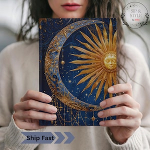 May include: A celestial-themed journal with a gold sun and crescent moon design on a dark blue background. The cover features intricate details and a starry night sky. The journal is held by a person.