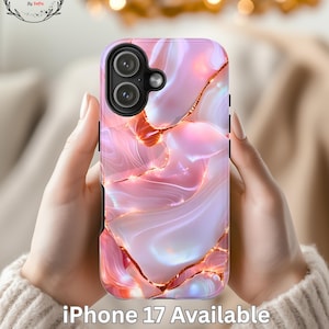 May include: Pink and gold iPhone 17 phone case with a marble design. The case has a glossy finish and features a dual-lens camera cutout. The text "iPhone 17 Available" is printed on the case.