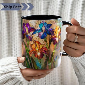 May include: Black ceramic mug with a colorful stained glass design of iris flowers. The design features shades of blue, purple, yellow, and orange.