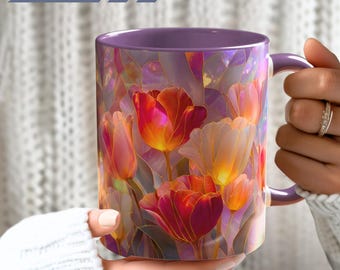 May include: A ceramic mug featuring a vibrant stained glass pattern of red, orange, and yellow tulips. The mug has a solid purple handle and interior rim. The exterior surface displays a colorful floral design with dark outlines.