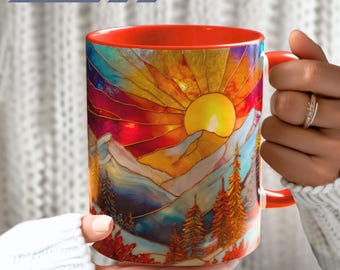 Könnte beinhalten: Ein Keramikbecher mit einem farbenfrohen Druck im Buntglas-Stil, der eine leuchtend gelbe Sonne über stilisierten Berggipfeln und Nadelbäumen zeigt. Der Becher hat ein einfarbig orangefarbenes Inneres und einen passenden orangefarbenen Henkel.