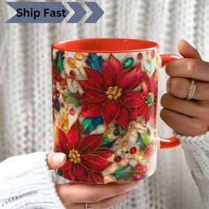 Könnte beinhalten: Ein Keramikbecher mit einem lebendigen Muster im Buntglas-Stil, das rote Weihnachtssterne, grüne Blätter und goldene Akzente zeigt. Der Becher hat ein einfarbig rotes Inneres und einen roten Henkel. Der Text Ship Fast ist oben links zu sehen.