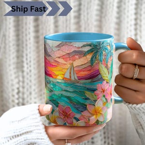 Könnte beinhalten: Ein Keramikbecher mit hellblauem Innenraum und Henkel, verziert mit einer farbenfrohen Illustration im Buntglas-Stil, die ein Segelboot auf dem Ozean bei Sonnenuntergang sowie tropische Palmenblätter und Frangipani-Blüten zeigt.