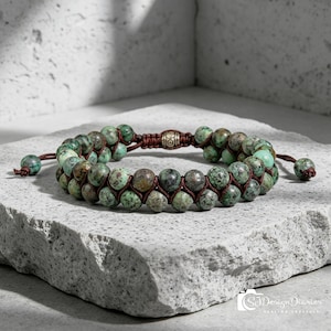 May include: Double-strand beaded bracelet featuring green and brown speckled stones. The beads are strung on a brown cord, with a decorative metal clasp and adjustable cord ends. A stylish accessory for everyday wear.