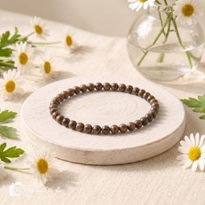 May include: A circular bracelet composed of small, round, dark brown wooden beads with a visible natural grain pattern. The beads are uniform in size and strung together to form a continuous loop, displaying a smooth, polished finish throughout.