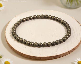 Könnte beinhalten: Ein Armband aus Pyritperlen mit kleinen, runden, metallischen Perlen. Das Armband wird auf einem hellen Holzuntersetzer präsentiert, mit dem Text "SJ Design Diaries Healing Crystals" oben links. Gänseblümchen und eine Blumenvase befinden sich im Hintergrund.