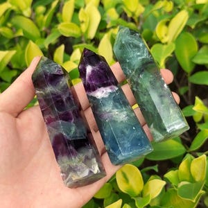 May include: Three fluorite crystal points in shades of green, purple, and blue. The crystals are smooth and polished, with a pointed tip and a flat base.