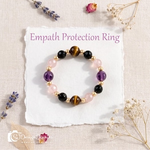 May include: A beaded ring featuring alternating round tiger's eye, black onyx, amethyst, and rose quartz beads separated by small gold-toned metal spacers. The text Empath Protection Ring is printed above the ring on a white textured paper background.