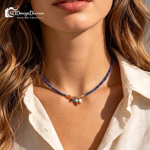 May include: A beaded necklace featuring small, faceted deep blue lapis lazuli stones. The center of the necklace is adorned with a cluster of dangling charms, including a white pearl, a bright turquoise bead, and small orange and blue stones.