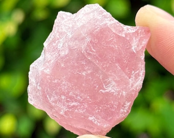 May include: A rough, pink rose quartz crystal with a natural, irregular shape. The crystal is translucent and has a light pink hue.