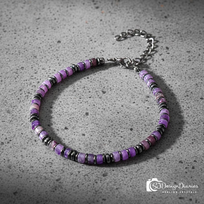 May include: A beaded bracelet featuring purple and black beads. The bracelet is made of small, round, purple beads interspersed with black metallic beads. The bracelet has a silver-colored chain and clasp for adjustable sizing. The bracelet is on a gray surface.
